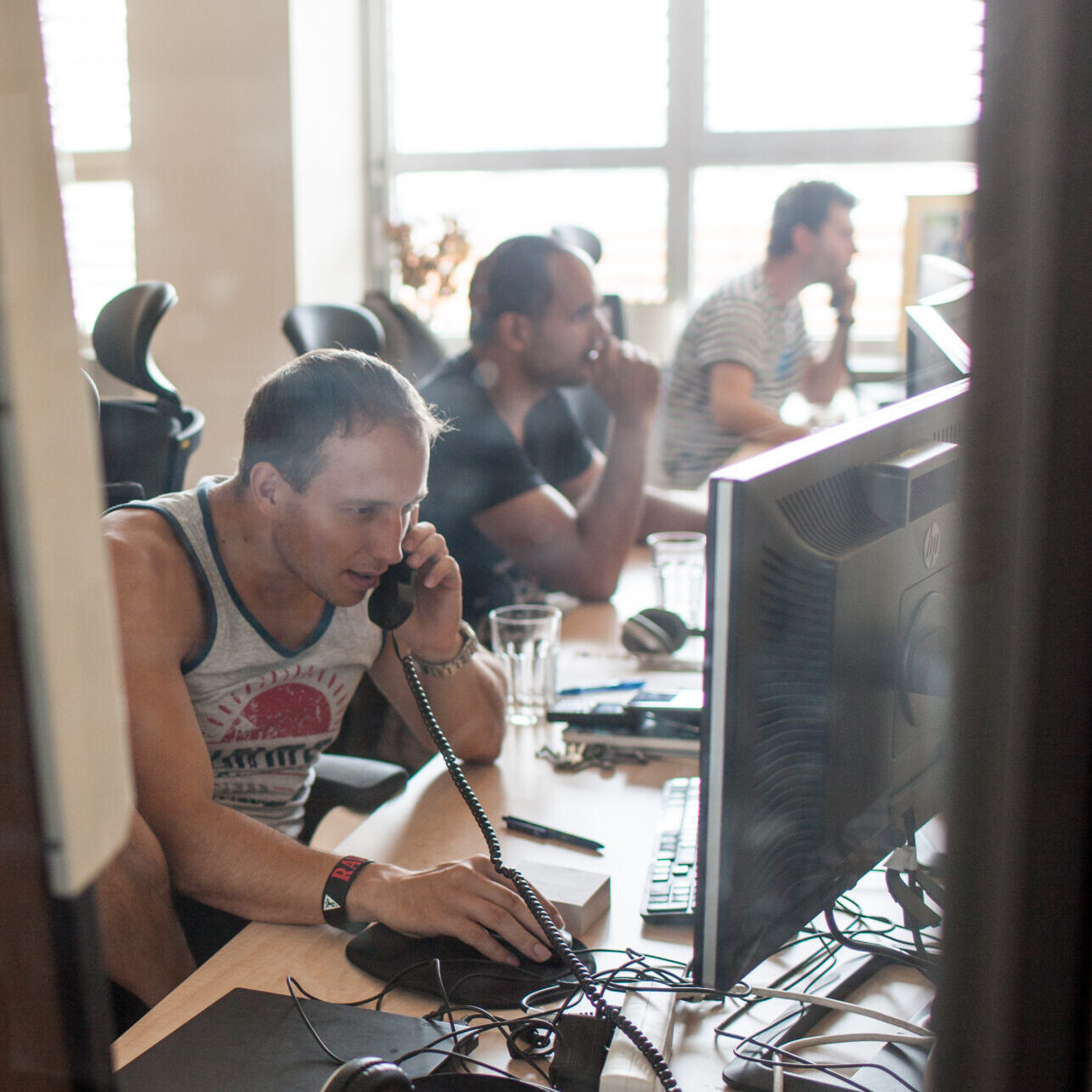 a group of men sitting at a desk with computers, one on a phone